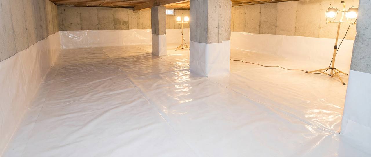 Heavy white 20-mil reinforced vapor barrier sealed across a crawl space floor and foundation walls